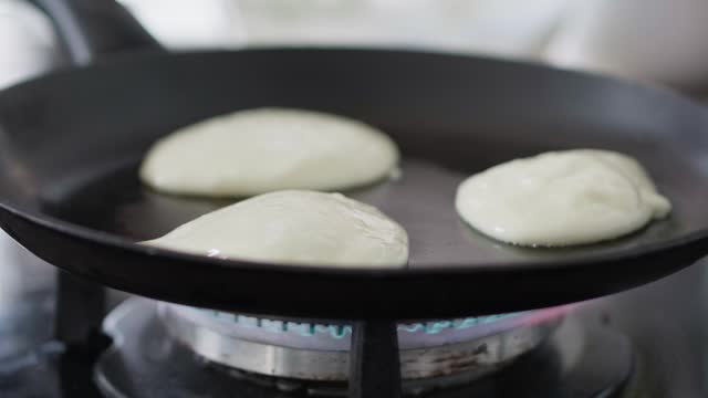 Woman making pancakes in a hot frypan in her kitchen for breakfast