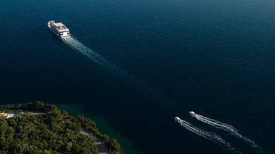 Aerial view of ferry and two small boats navigating and leaving bright trail on deep sea background. Photo taken from above with drone