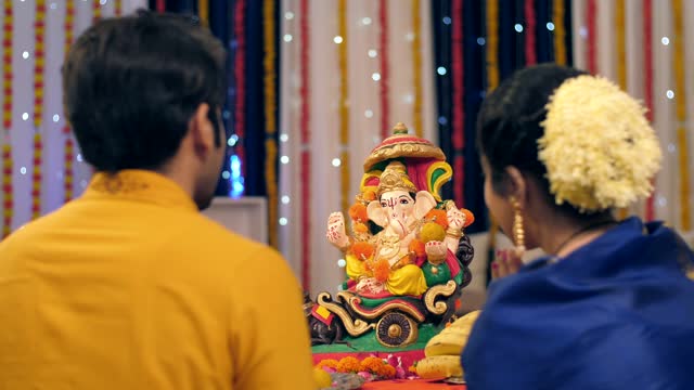 Husband and wife offering flowers to Lord Ganesh's idol on Ganesh Chaturthi, festival celebration
