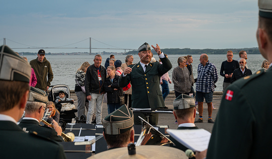 August 30, 2023, Fredericia, Denmark, a conductor of a military standing in front of the lillebælt bridge … smiles at his musicians