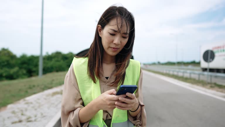 Young woman with reflective west text messaging for help for her broken vehicle on highway