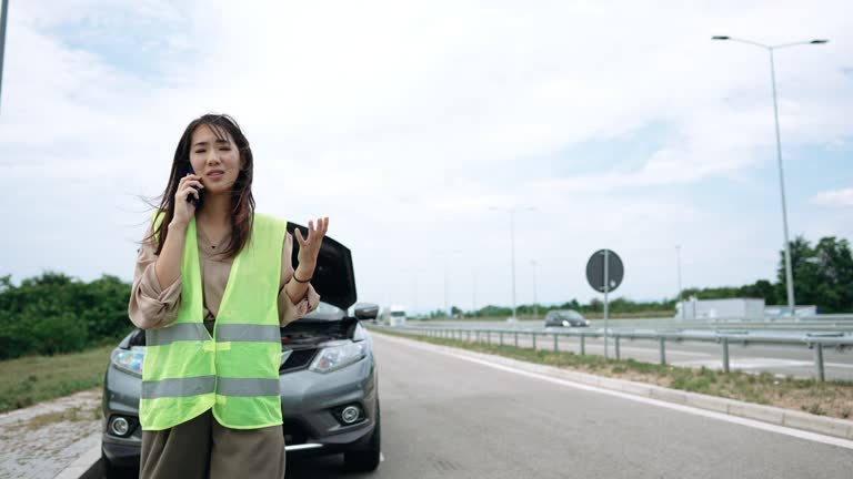 Young woman with reflective west calling help for her broken vehicle on highway