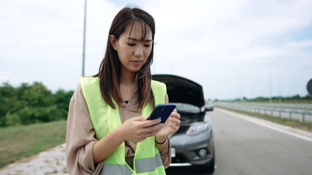 Young woman with reflective west text messaging for help for her broken vehicle on highway