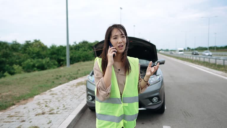 Young woman with reflective west calling help for her broken vehicle on highway