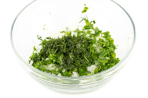Fresh chopped dill, parsley and onion in a glass bowl on a white background. Copy space.