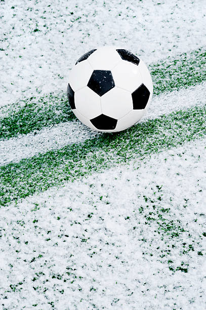 A snow covered Soccer Ball sitting at the halfway line with the line cleared of snow