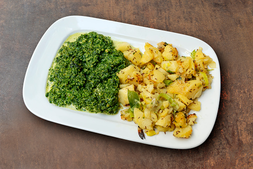 Rectangular dish with chopped spinach and potatoes and spring onion on rough background