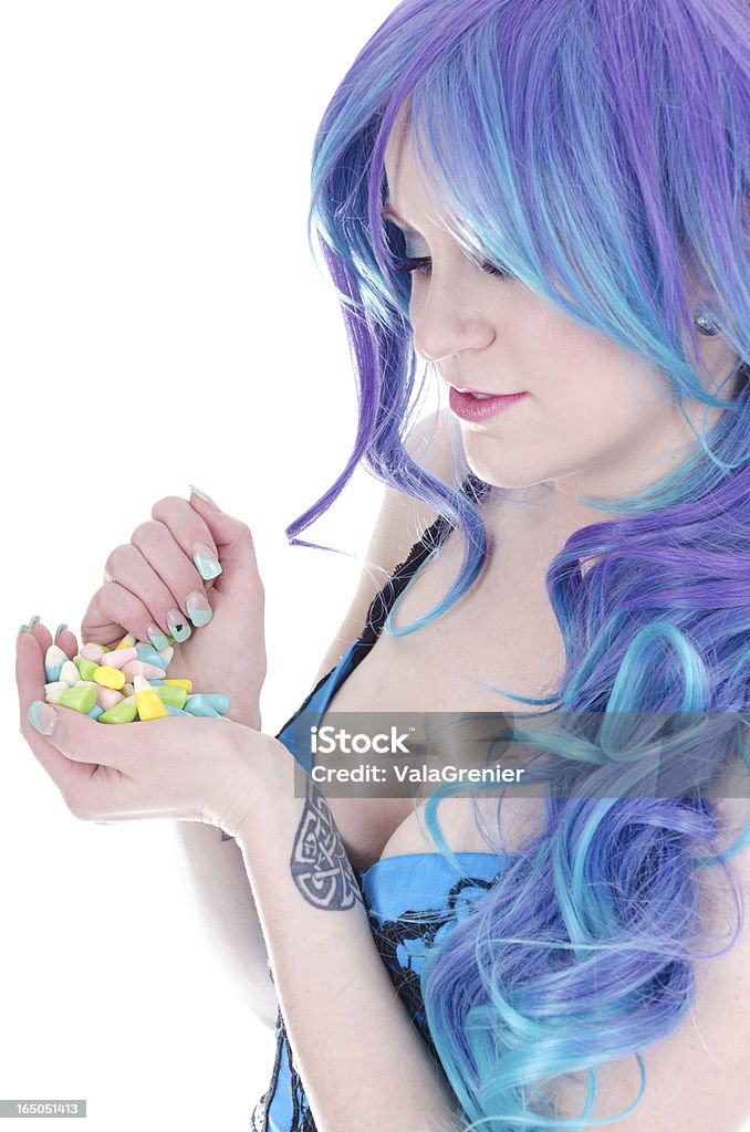 Blue/purple haired woman with Easter candy. Vertical studio shot on white of woman with blue/purple wig holding Easter coloured candy corn. Corset Stock Photo