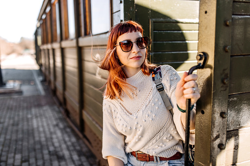 Young smiling woman with sunglasses standing out of the old tourist train, getting ready for ride