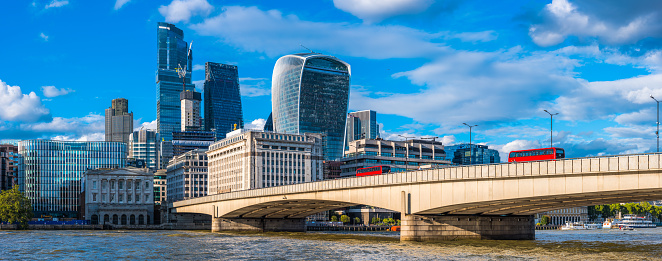 Red double decker buses driving across London Bridge to the modern skyscrapers of the City Financial District.