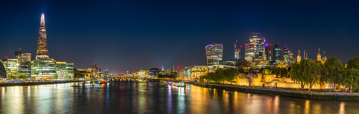 Panoramic view along the River Thames at dusk reflecting the illuminated skyscrapers of the City of London opposite City Hall and The Shard in the heart of the UK's vibrant capital city.