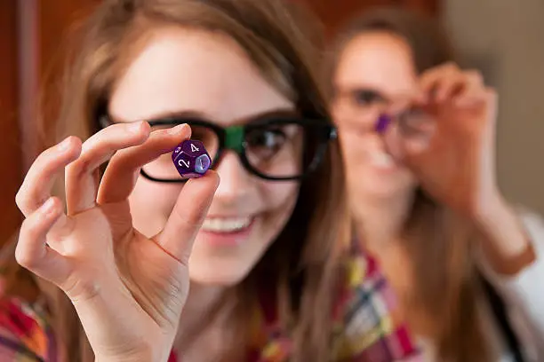 Cute and nerdy girls play role playing dice game. Here they examine and show of their dice. Part of an extensive lifestyle series of images of multi-ethnic teens hanging out together and playing cards and dice games.