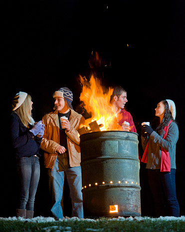 These charming All-American looking young adults are enjoying a warm campfire in a 50 gallon barrel and each others company as they sip hot cocoa. Some grain.