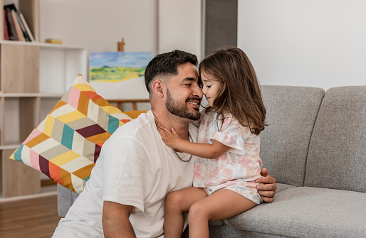 Latin American family father with little daughter showing affection on the sofa - daughter kisses her father -