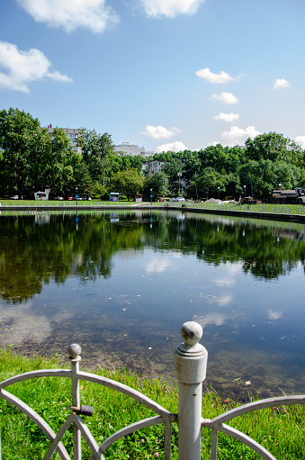 A pond surrounded by a monument and green trees with a lawn. High quality photo