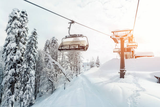 remontée mécanique vide ropeway sur hilghland montagne alpine station d’hiver le soir ensoleillé lumineux. ski télésiège câble façon avec les gens aiment le ski et le snowboard. ciel rétroéclairé de coucher du soleil brillant sur l’arrière- - frozen ice sky sun photos et images de collection