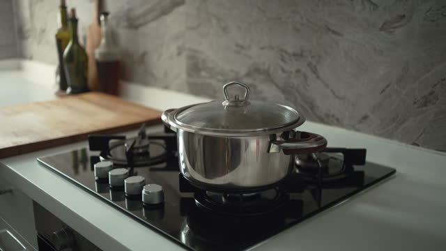 Cooking pot with its lid on, sits on a lit gas burner creating steam as it heats