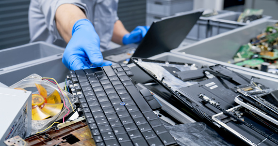 Repairman reaching for laptop keyboard while repairing at recycling centre.