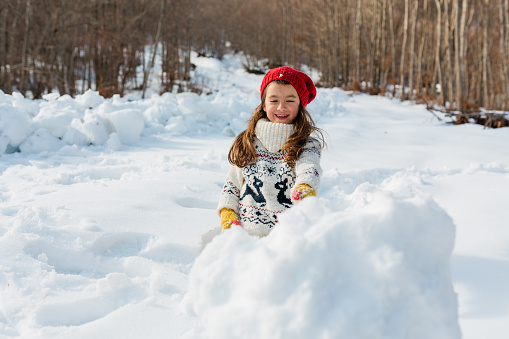 Playful Little girl rolling snowball , building a Snowman in the nature