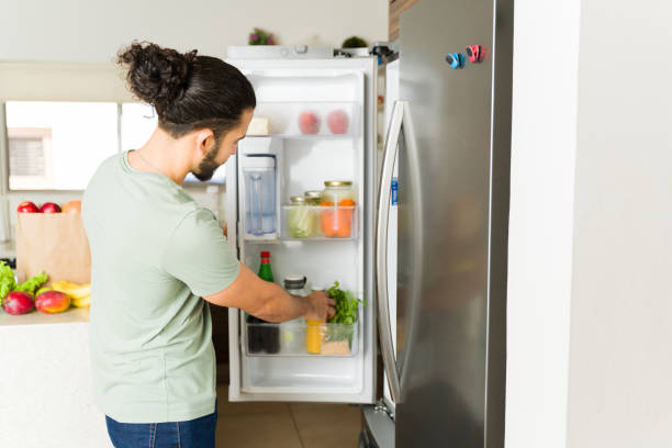 istock Latin young man opening the fridge in the kitchen and organizing the groceries while doing house chores looking happy 1650651295
