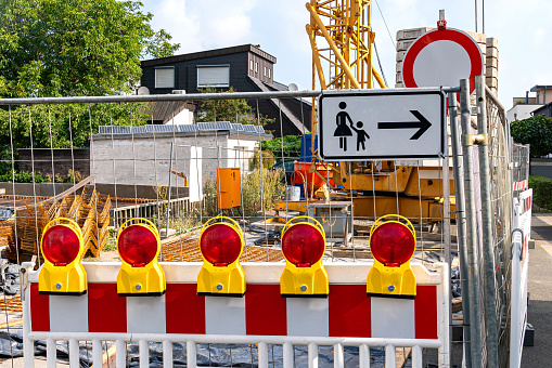 Construction site with tower crane fenced with white and red barriers with red signal lights.