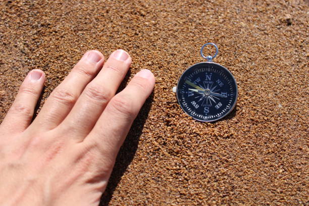 brújula de dirección y mano masculina en la arena de la playa. foto temática de ayuda - compass exploration the way forward beach fotografías e imágenes de stock