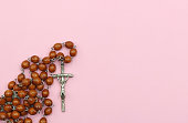 A brown Christian rosary on a pink background. Space for text
