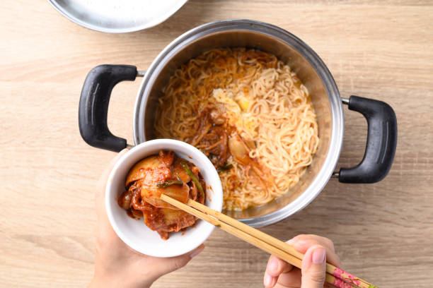 Korean spicy instant noodles soup with kimchi and egg in hot pot eating by use chopsticks stock photo