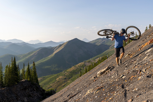 Male mountain biker carries bike up steep slope