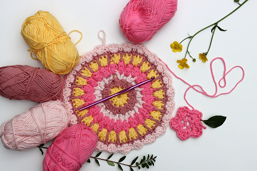 Pink balls of cotton yarn, crochet pattern and flowers on white background with copy space. Beautiful spring crochet ideas
