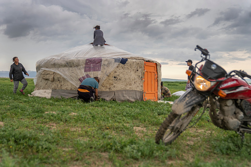 Ovorkhangai Province, Mongolia — July 19, 2023: A motorcycle is parked before nomadic people building a ger (yurt) on an overcast day.