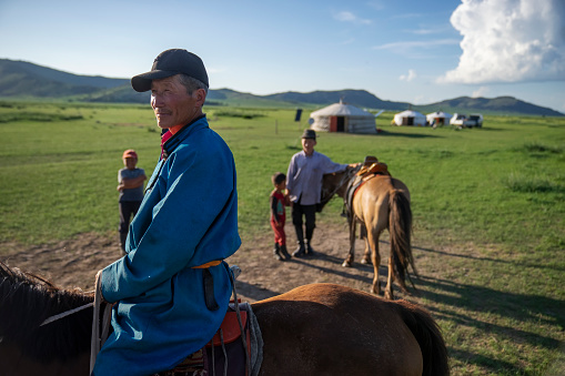 Bulgan Province, Mongolia - July 16, 2023: Multi-generational members of a nomadic family around horses gather in front of gers (yurts).