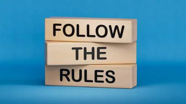 Photo of Follow the rules symbol. Concept words Follow the rules on wooden blocks. Business and follow the rules concept. Copy space.3D rendering on blue background.