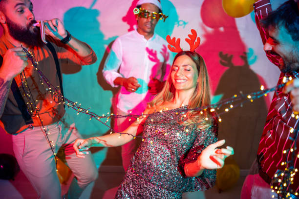Group of cheerful young friends having fun doing limbo dance passing under Christmas lights at New Year Eve party