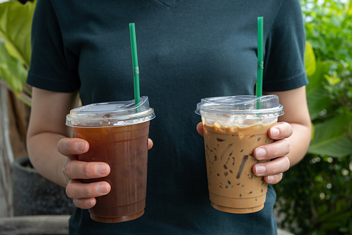 Cropped shot view of woman hand holding a plastic cups of iced milk coffee with iced Americano.