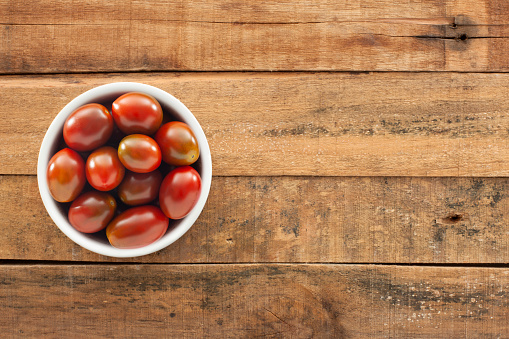 Top view of white bowl full of cherry tomatoes over wooden table