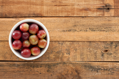 Top view of white bowl full of red grapes over wooden table