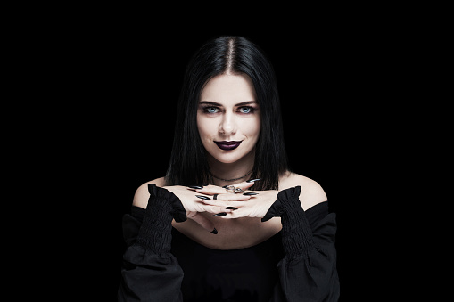 Perfect soothsayer woman with black hair, lips and nails looking at camera on black background