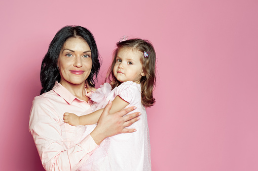 Adorable mom with child baby girl studio portrait. Happy smiling mother and daughter little baby on pink background
