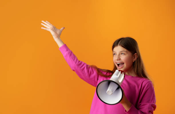 Teen girl making announcement with megaphone on yellow background Teen girl making announcement with megaphone on yellow background in studio speaker of the house stock pictures, royalty-free photos & images