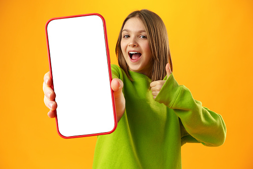 Teen girl showing smartphone screen with copy space over yellow background in studio