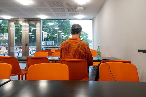 Stockholm, Sweden July 15, 2023 A man dressed in an orange sweater is color coordinated with the chairs in a snack bar.
