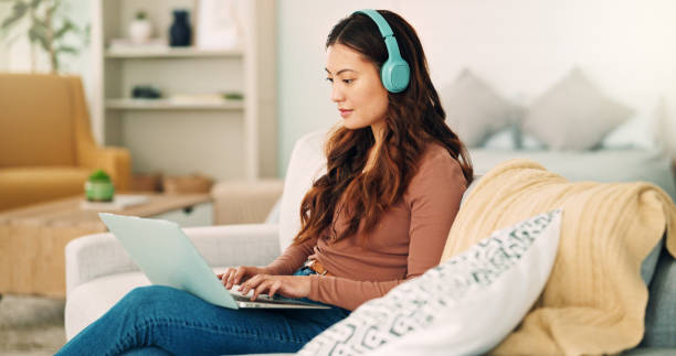 lavoro online, musica su internet e donna che ascolta un podcast audio mentre digita un'e-mail sul divano del soggiorno di casa. imprenditore remoto che lavora sul laptop con la radio sul web sul divano - domestic staff audio foto e immagini stock