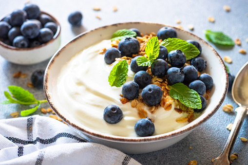 Greek Yogurt with granola and fresh bluebery at light stone table. Close up image.