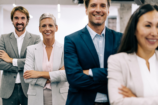 Portrait of beautiful smiling businesswoman with her colleagues. Multi-ethnic group of business persons standing in a row in modern office. Successful team leader and her team in the office. Selective focus on one of them.