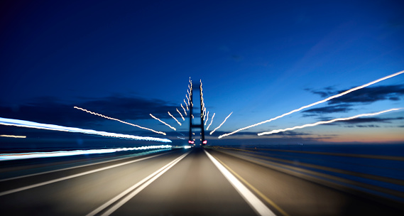 Light trails on road. High speed driving makes abstract light trails at dusk. Entering suspension bridge \