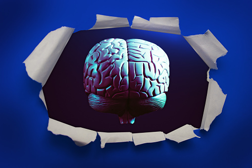 Low-key, anatomically correct brain model bursts through a sheet of bright blue paper, with curled and ripped edges.