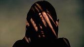 Woman covers her face with her hands. There are striped shadows on the face. Studio shot.