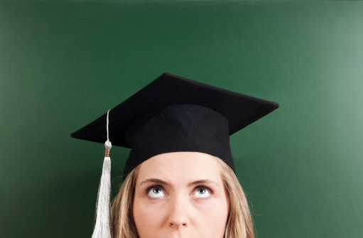 Thinking young woman student wearing cap in front of  empty blackboard