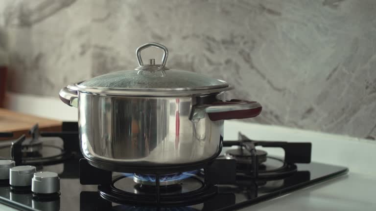 Cooking pot with its lid on, sits on a lit gas burner creating steam as it heats